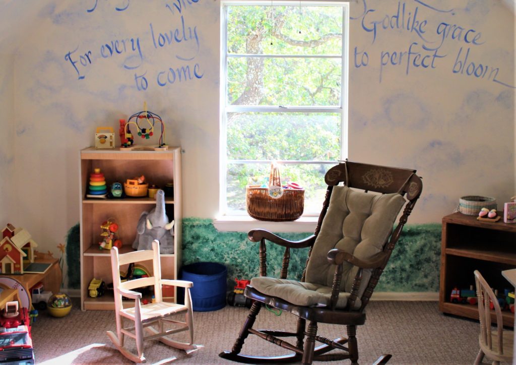 a bright children's room with shelves full of colorful toys, and a pair of rocking chairs, one large and one small at center.
