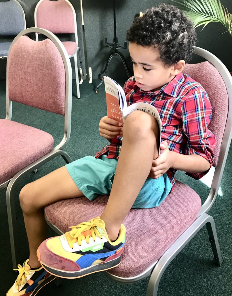 child sitting in a chair reading a small booklet about the Bible